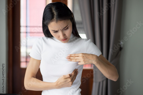 Serious asian woman checking her breast at home, concept of breast cancer awareness month, breast cyst or tumor inspection, body care, precautionary and preventive medicine