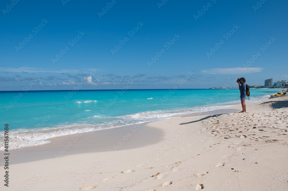 A tourist on a beach in Cancun, Mexico, takes a picture of the turquoise sea. In the background the a blue sky and few clouds. An ideal place to relax with nature.