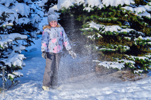 The girl plays with snow. Child rejoices in winter. Happy childhood.