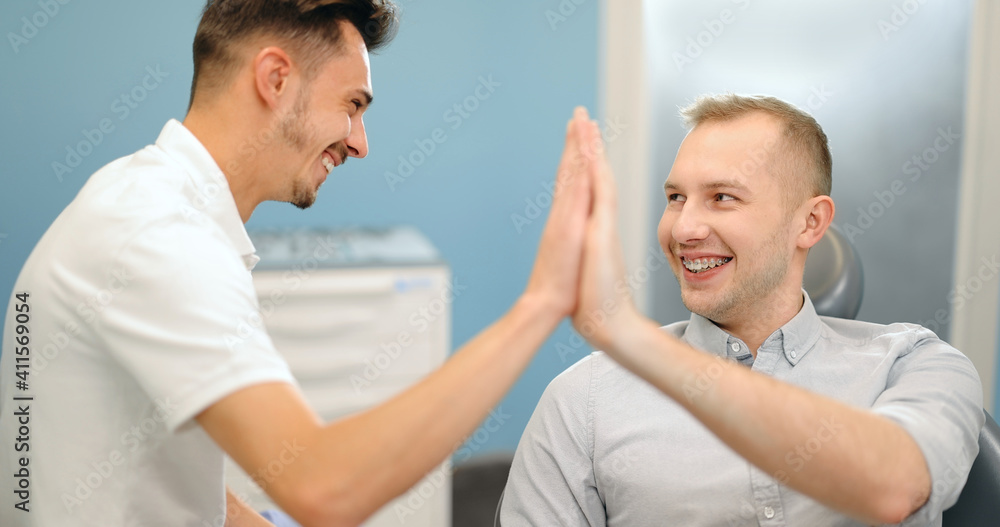 Fototapeta premium Happy male patient giving five to the doctor during a regular orthodontic visit at the dental office. Happy dental treatment concept. 4k video screenshot, please use in small size