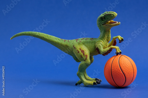 Green dinosaur toy with basketball ball. Basketball minimal card blue background. © dvulikaia