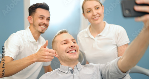 Young male patient in dental braces making selfie photo with a dentist and assistant during a regular orthodontic visit at the dental office. 4k video screenshot, please use in small size