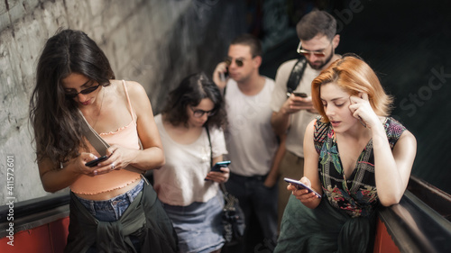 Group of friends talk on smartphones while standing on escalator. Modern people with cell phones outdoor. Mobile communication technology. High angle view