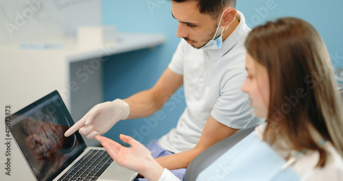 Dentist showing photo of teeth on a laptop for a young patient during an orthodontic treatment. Girl having a consultation with an orthodontist. 4k video screenshot, please use in small size © rh2010