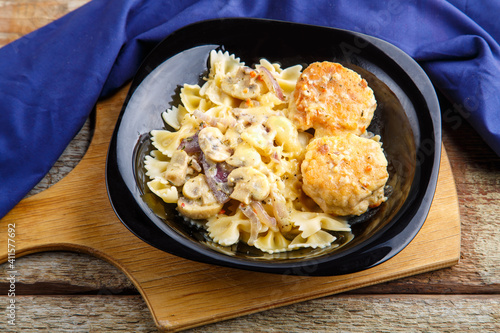 Pasta in a creamy sauce with mushrooms and chicken meatballs in a plate on a board on a blue napkin.
