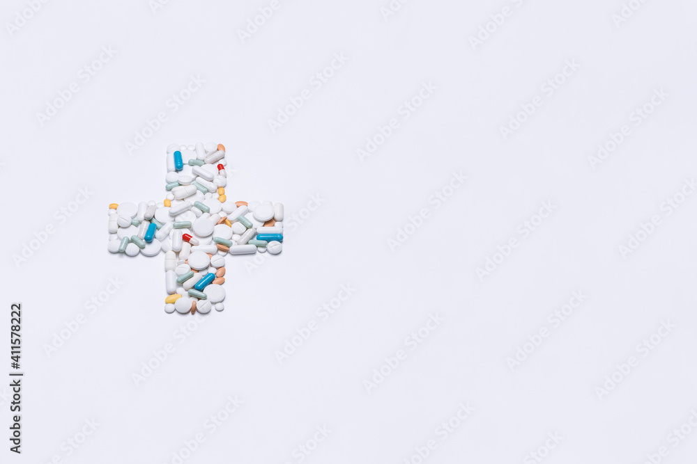 Plus symbol formed with drug pills, drugs presented in the form of capsules, dragees and pills from the pharmaceutical industry that form the plus symbol, on white background.