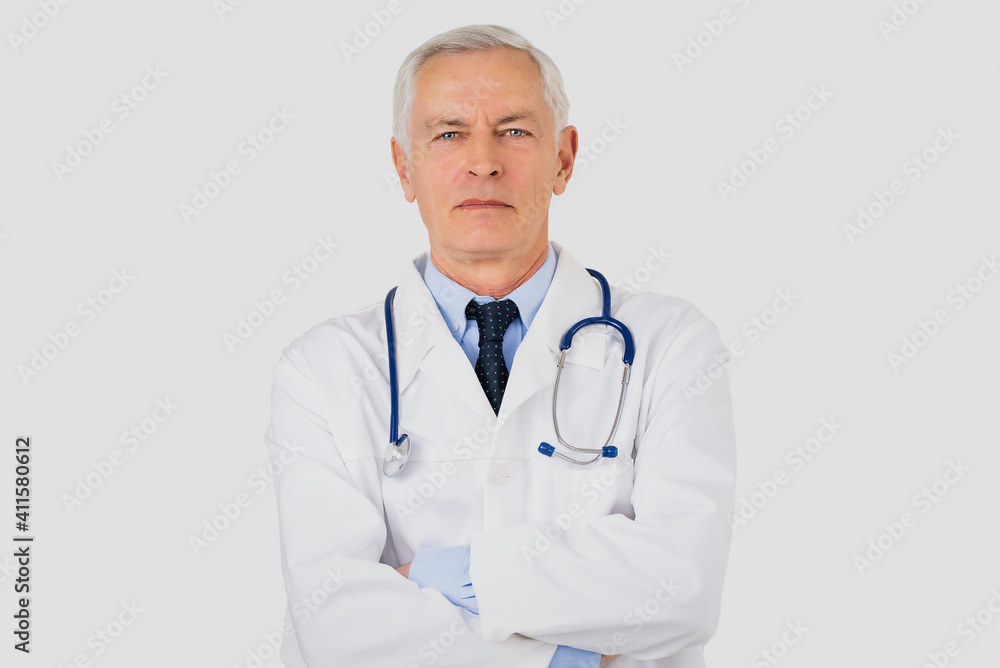 Portrait shot of serious faced male doctor standing with arms crossed at isolated background
