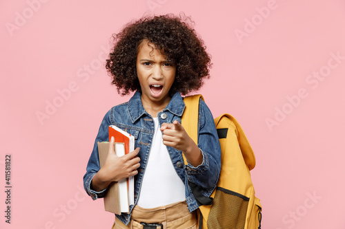 Indignant angry little african kid school girl 12-13 years old in casual clothes backpack hold book pointing index finger camera on you isolated on pastel pink background Childhood education concept.