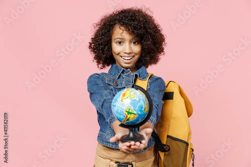 Friendly little african american kid school girl 12-13 years old in casual clothes backpack hold in palm giving Earth world globe isolated on pastel pink background studio Childhood education concept