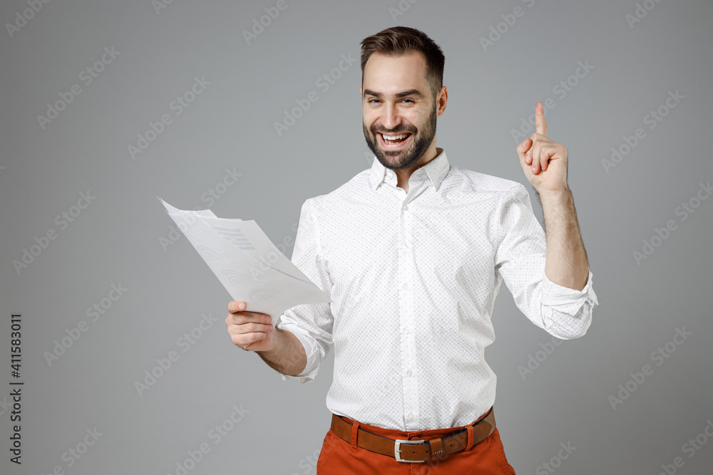Excited young bearded business man in classic white shirt hold papers document hold index finger up with great new idea isolated on grey background studio portrait. Achievement career wealth concept.
