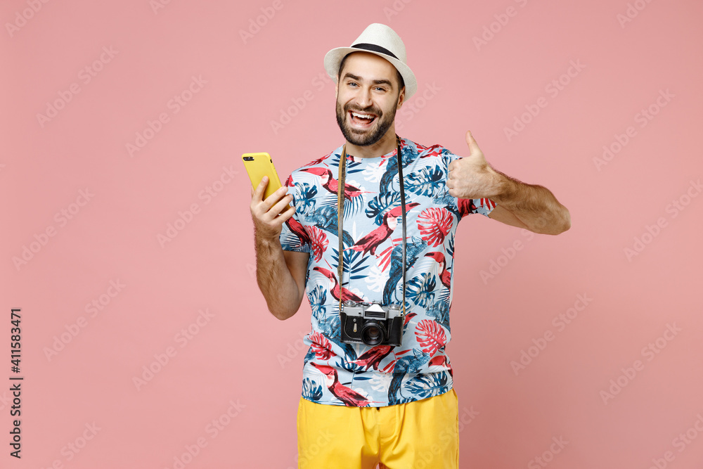 Funny traveler tourist man in summer clothes, hat using mobile cell phone typing sms message showing thumb up isolated on pink background. Passenger traveling on weekends. Air flight journey concept.