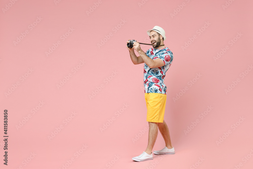 Full length side view of funny traveler tourist man in summer clothes hat taking pictures on vintage photo camera isolated on pink background. Passenger travel on weekends. Air flight journey concept. Full length side view of funny traveler tourist man in summer clothes hat taking pictures on vintage photo camera isolated on pink background. Passenger travel on weekends. Air flight journey concept.