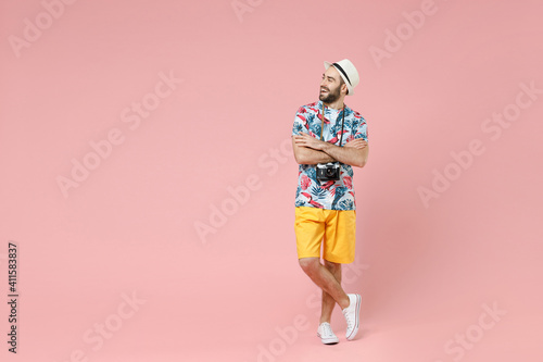 Full length of cheerful young traveler tourist man in summer clothes hat holding hands crossed looking aside isolated on pink background. Passenger traveling on weekends. Air flight journey concept.