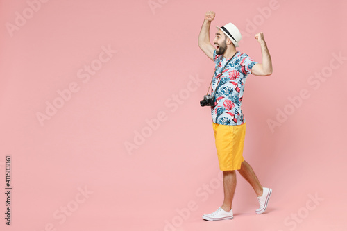 Full length side view of excited traveler tourist man in summer clothes hat doing winner gesture celebrating isolated on pink background. Passenger traveling on weekends. Air flight journey concept.