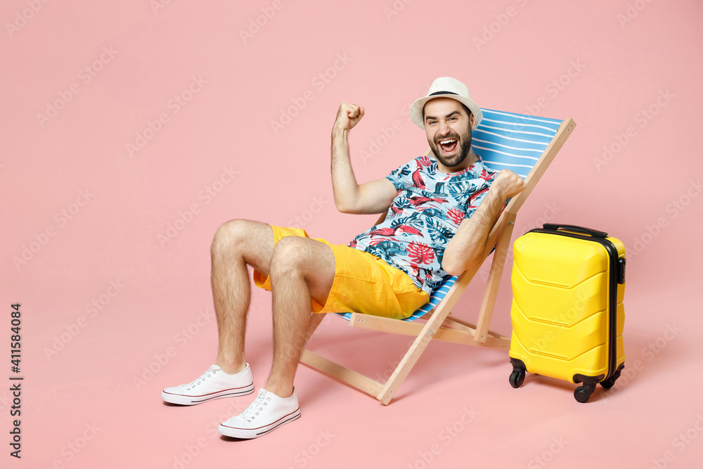 Full length happy young traveler tourist man in summer clothes hat sit on deck chair clenching fists like winner isolated on pink background. Passenger travel on weekend. Air flight journey concept. - obrazy, fototapety, plakaty 