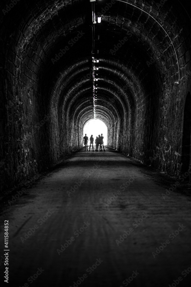 silhouettes of human beings in backlight at the end of a dark tunnel