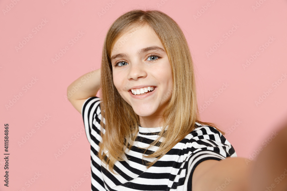 Close up little blonde smiling happy cute kid girl 12-13 years old wearing striped oversized t-shirt doing selfie shot on mobile phone isolated on pink background children Childhood lifestyle concept. Close up little blonde smiling happy cute kid girl 12-13 years old wearing striped oversized t-shirt doing selfie shot on mobile phone isolated on pink background children Childhood lifestyle concept.