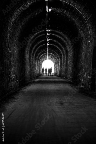 silhouettes of human beings in backlight at the end of a dark tunnel