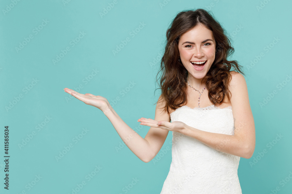 Cheerful excited laughing bride young woman 20s in beautiful white wedding dress pointing hands aside isolated on blue turquoise color background studio portrait. Ceremony celebration party concept. Cheerful excited laughing bride young woman 20s in beautiful white wedding dress pointing hands aside isolated on blue turquoise color background studio portrait. Ceremony celebration party concept.