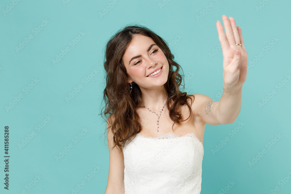 Smiling pretty bride young woman 20s in beautiful white wedding dress looking at hand finger with ring isolated on blue turquoise color background studio portrait. Ceremony celebration party concept. Smiling pretty bride young woman 20s in beautiful white wedding dress looking at hand finger with ring isolated on blue turquoise color background studio portrait. Ceremony celebration party concept.