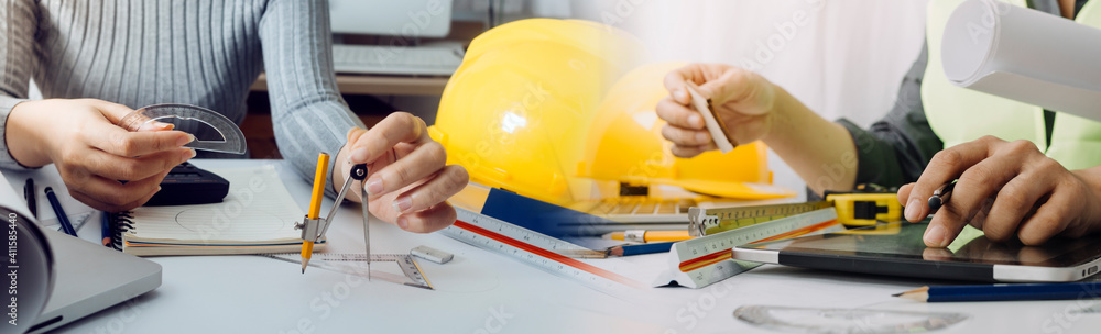 Two colleagues discussing data working and tablet, laptop with on on architectural project at construction site at desk in office Two colleagues discussing data working and tablet, laptop with on on architectural project at construction site at desk in office