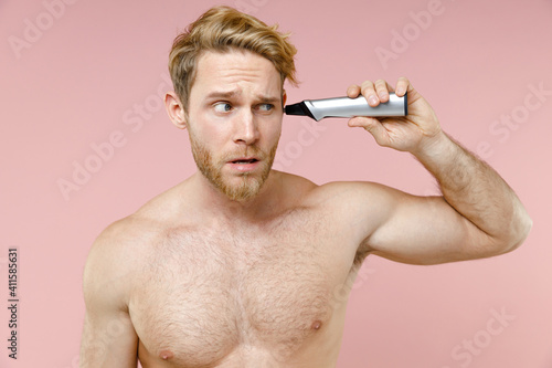 Puzzled bearded naked young man 20s years old perfect skin hold electric nose and ear trimmer isolated on pastel pink background studio portrait. Skin care healthcare cosmetic procedures concept.