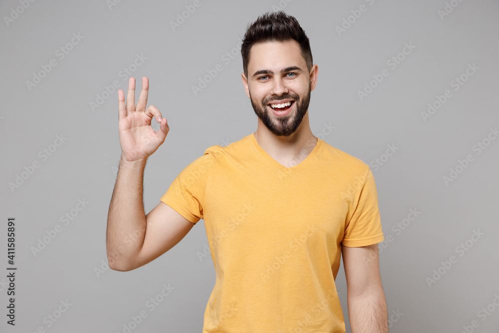 Young caucasian european happy bearded satisfied attractive man 20s wearing casual yellow basic t-shirt show ok okay gesture isolated on grey color background studio portrait People lifestyle concept. Young caucasian european happy bearded satisfied attractive man 20s wearing casual yellow basic t-shirt show ok okay gesture isolated on grey color background studio portrait People lifestyle concept.