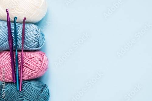 Fényképezés Multicolored crochet hooks with balls of yarn on a blue background with copy space