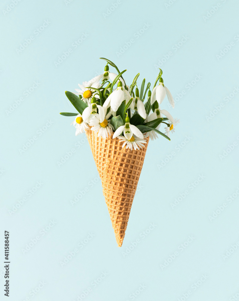 White spring flowers blooming out of an ice cream cone against a pastel blue background. Minimal creative nature concept.