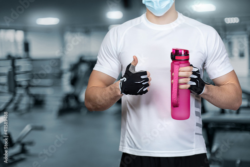 Athlete stands with bottle of water and shows good with hand gesture .