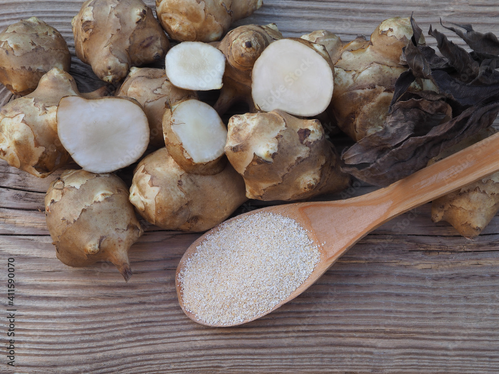 Fototapeta premium Fruits of the Jerusalem artichoke plant and natural powder with inulin on wooden table, top view. Healthy helianthus tuberosus root vegetables and dietary supplement for diabetes prevention 