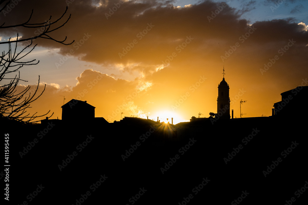 Silhouette of the town of Alfauir, in a beautiful sunset, with a cloudy sky and orange light.