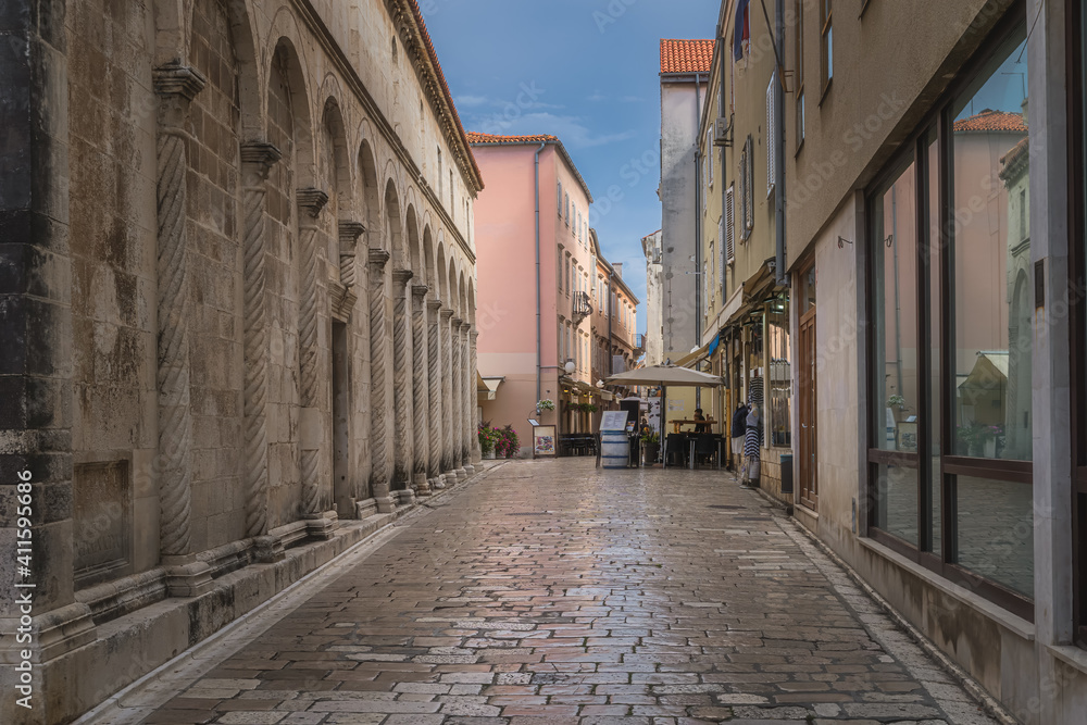 Tourists dining in outdoor restaurants in narrow streets of the old town district, surrounded by ancient Romanesque architecture, Zadar, Croatia