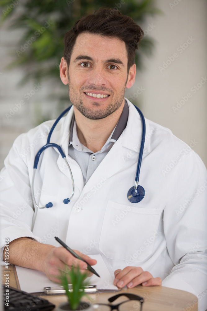 young doctor writing report while smiling to the camera young doctor writing report while smiling to the camera
