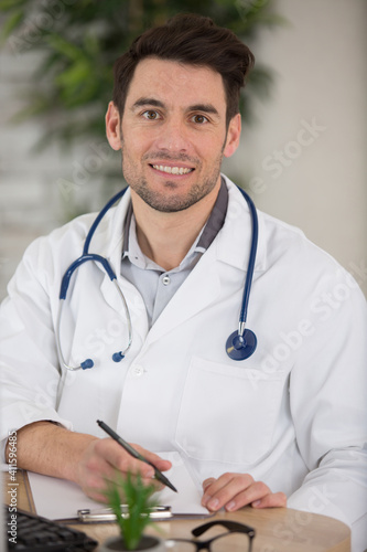 young doctor writing report while smiling to the camera