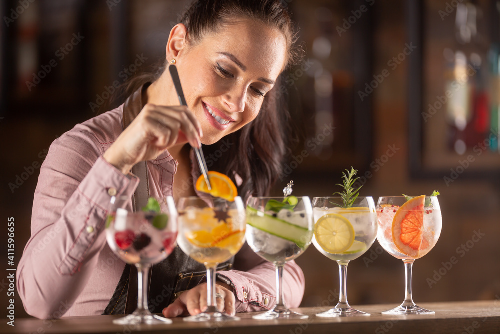 Bartender loving her job decorates gin tonic cocktails in glasses on a bar