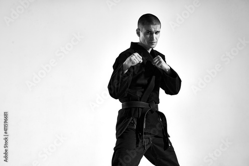 Canvas-taulu Confident male in kimono fighter posing in karate stance on studio background wi