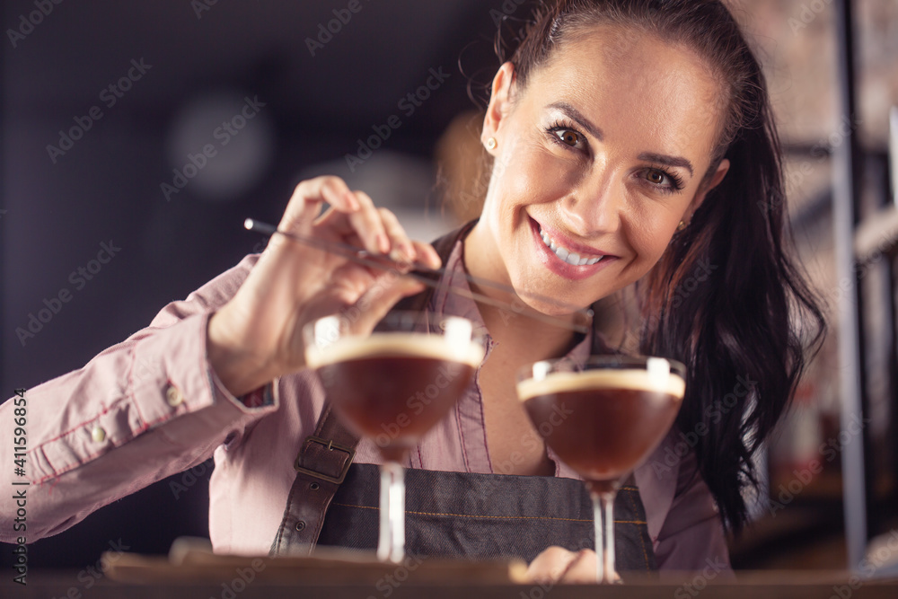 Young barmaid smiles after making two espresso martini short drinks with a coffee Young barmaid smiles after making two espresso martini short drinks with a coffee