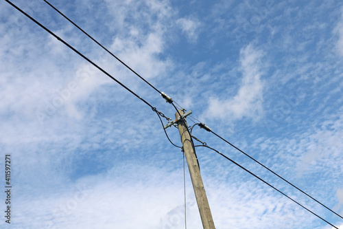 Old wooden power pole with power lines against blue cloudy sky