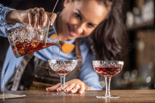 Quadro su tela Female bartender pours manhattan cocktail into an ornamental glass