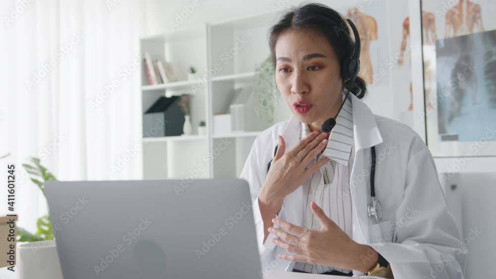 Young Asia lady doctor in white medical uniform with stethoscope using computer laptop talking video conference call with patient at desk in health clinic or hospital. Consulting and therapy concept. Young Asia lady doctor in white medical uniform with stethoscope using computer laptop talking video conference call with patient at desk in health clinic or hospital. Consulting and therapy concept.