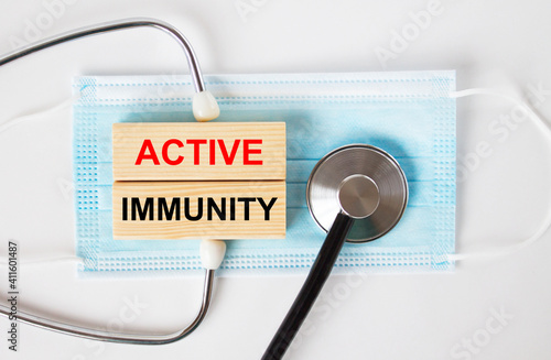 Wooden blocks with text Active Immunity lying on the mask and a stethoscope