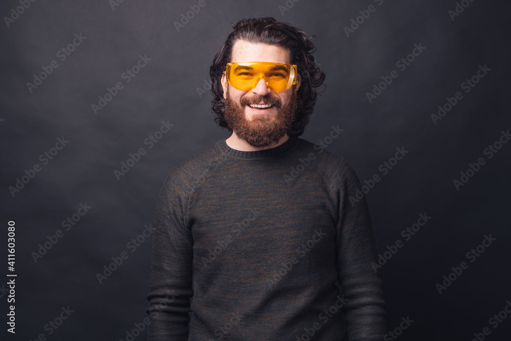 Portrait of handsome bearded man over black background wearing big yellow glasses.