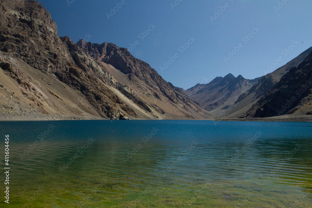 The colorful lake called Inca Lagoon in the Andes mountain range. The blue glacier water and yellow shallows surrounded by rocky mountains. 