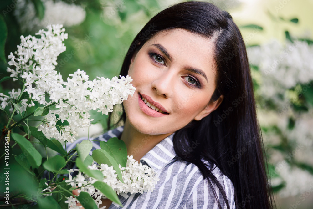 Portrait of a beautiful brunette whith a flowering tree. A young smiling woman against the background of spring blooming apple trees Portrait of a beautiful brunette whith a flowering tree. A young smiling woman against the background of spring blooming apple trees