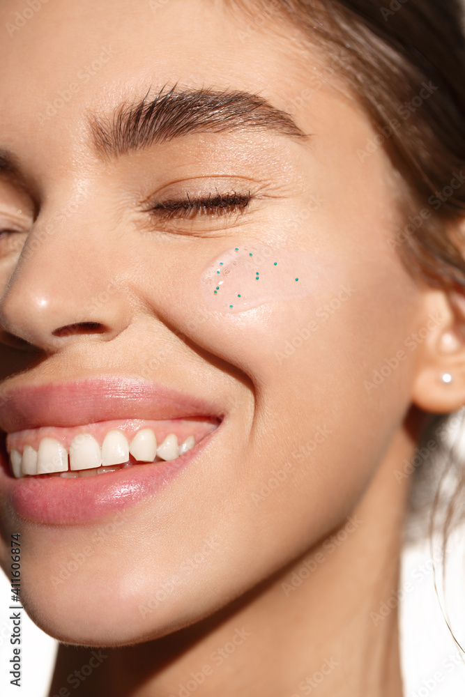 Fototapeta premium Skincare beauty. Young woman with happy smile, using facial hydrate skin product. Girl with no makeup, applying scrub or face cream with collagen and tea tree leaf ingredients. Close up