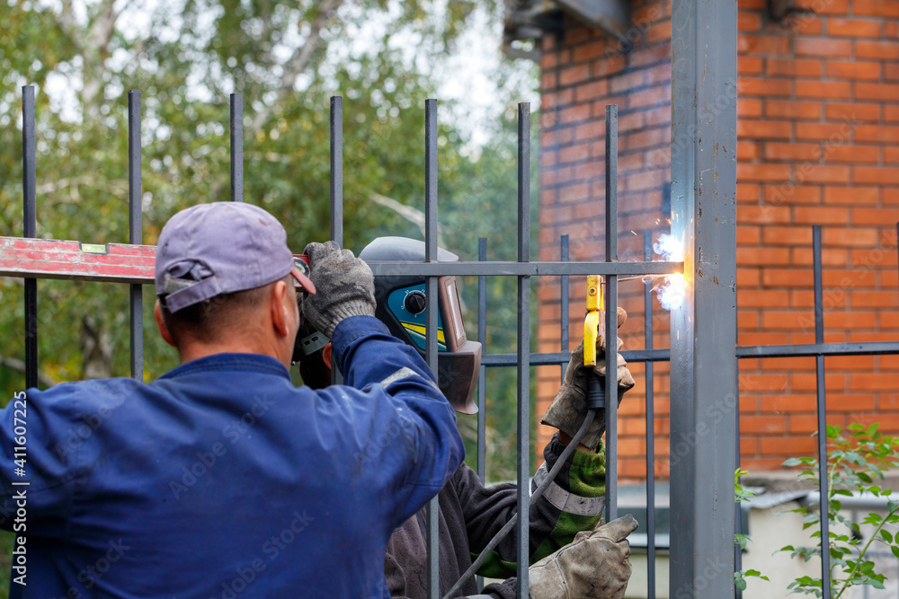 A team of construction workers install a metal fence around a new home.