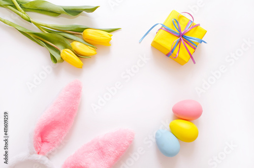 yellow tulips and colorful Easter eggs gift box, rabbit ears on a white background, top view.