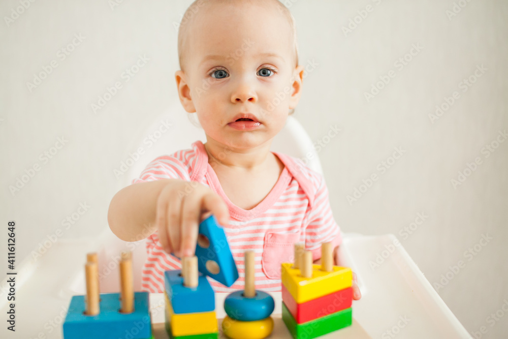little girl plays with an educational toy - a multi-colored wooden pyramid. Development of fine motor skills and logical thinking. High quality photo little girl plays with an educational toy - a multi-colored wooden pyramid. Development of fine motor skills and logical thinking. High quality photo