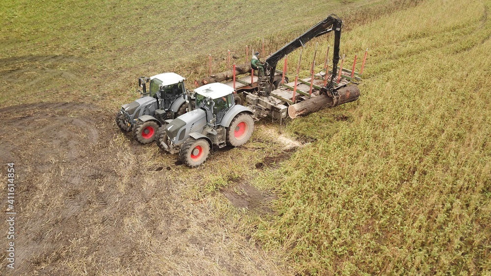 Traktoren mit Greifer verlädt einen gefällten Baum auf einen Anhänger, Forstwirtschaft / Landwirtschaft aus der Vogelperspektive Traktoren mit Greifer verlädt einen gefällten Baum auf einen Anhänger, Forstwirtschaft / Landwirtschaft aus der Vogelperspektive